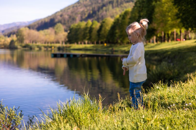 Ein kleines Mädchen mit Pferdeschwanz wirft kleine Steine in den See.