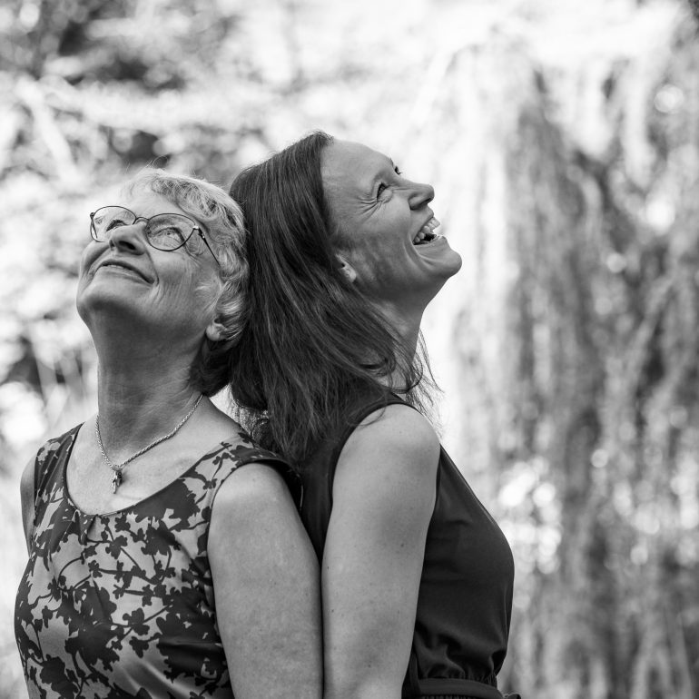 Ältere Mutter und Kind stehen Rücken an Rücken und schauen lachend nach oben