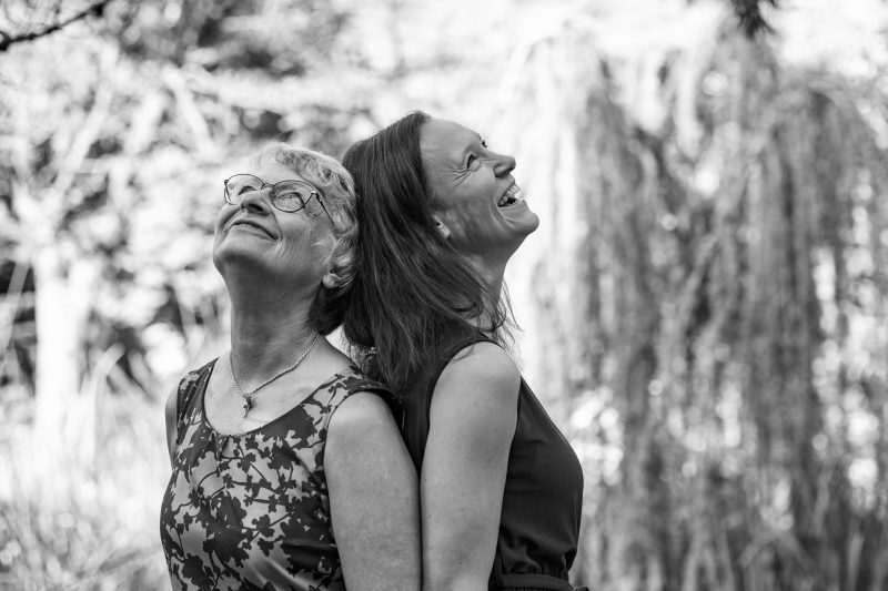 Ältere Mutter und Kind stehen Rücken an Rücken und schauen lachend nach oben