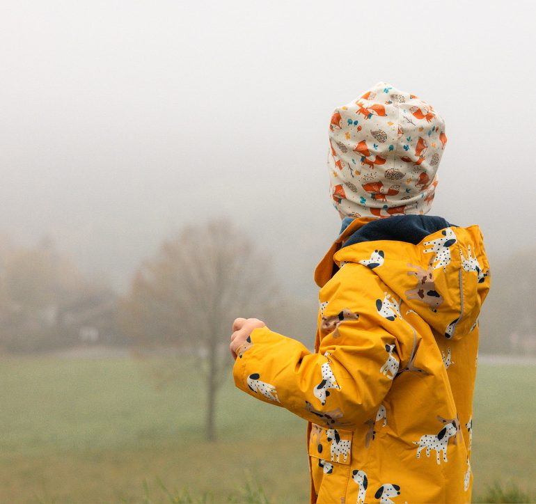 Kind in gelber Jacke schaut hinaus in den Nebel